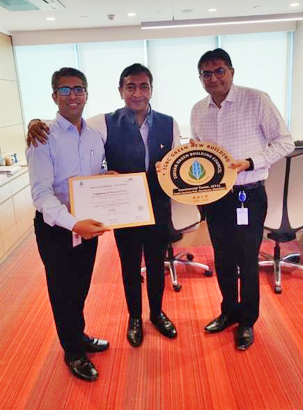 Three men in an office proudly holding an IGBC Green New Building award and a certificate.