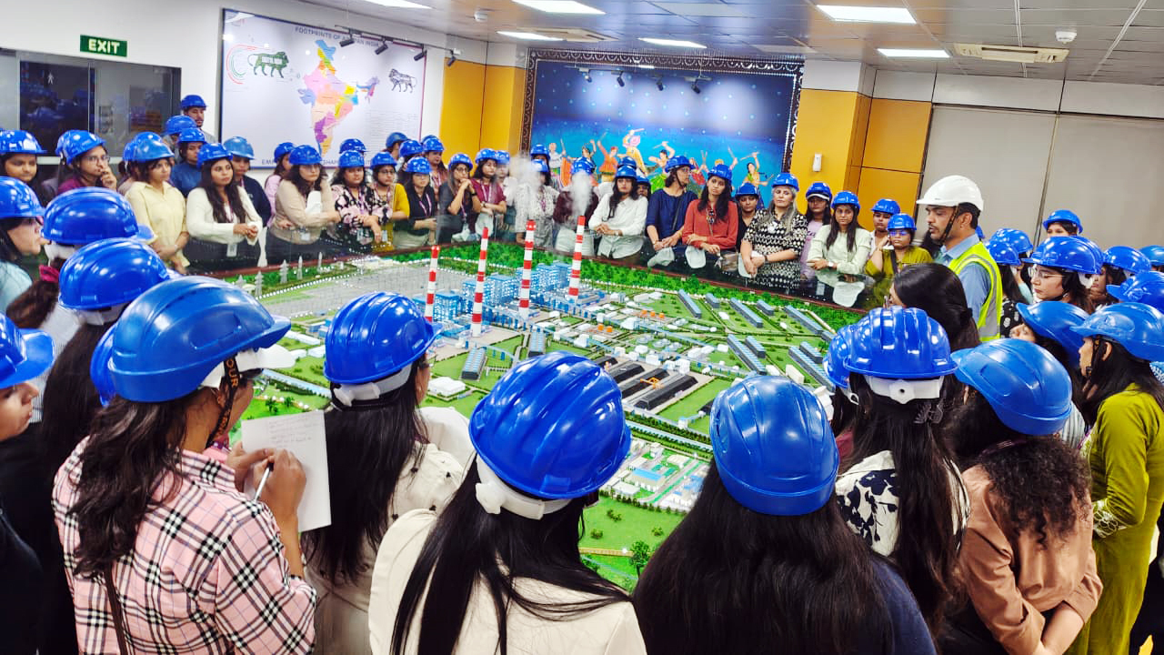 People in blue hard hats view an industrial plant model, while a guide explains details.
