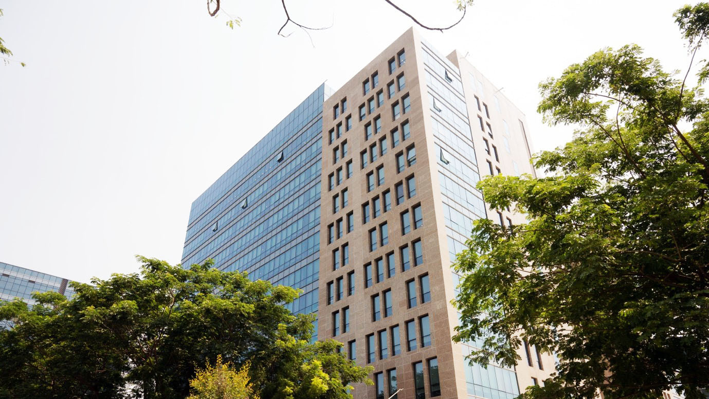Modern building with glass and stone, framed by green trees against a bright sky.