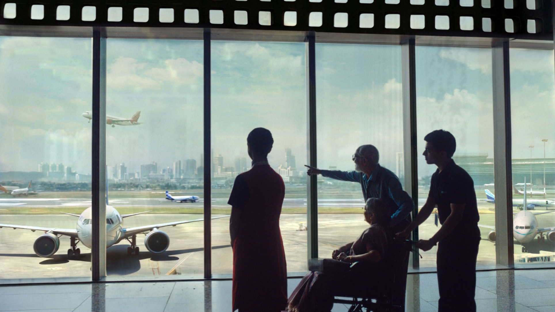 Silhouettes at an airport window watching planes, with a film strip border on top.