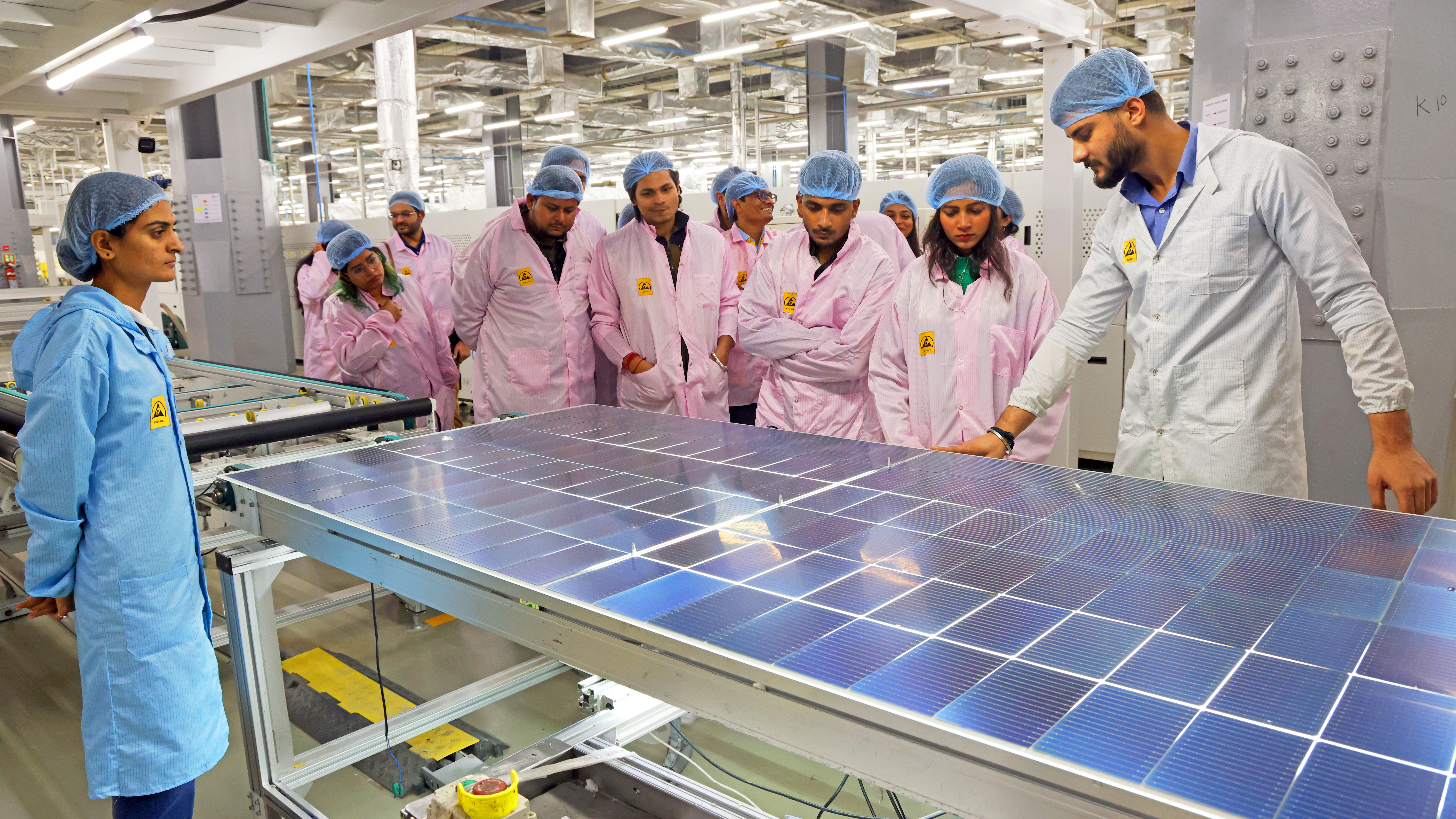 People in cleanroom attire observe a solar panel in a factory.
