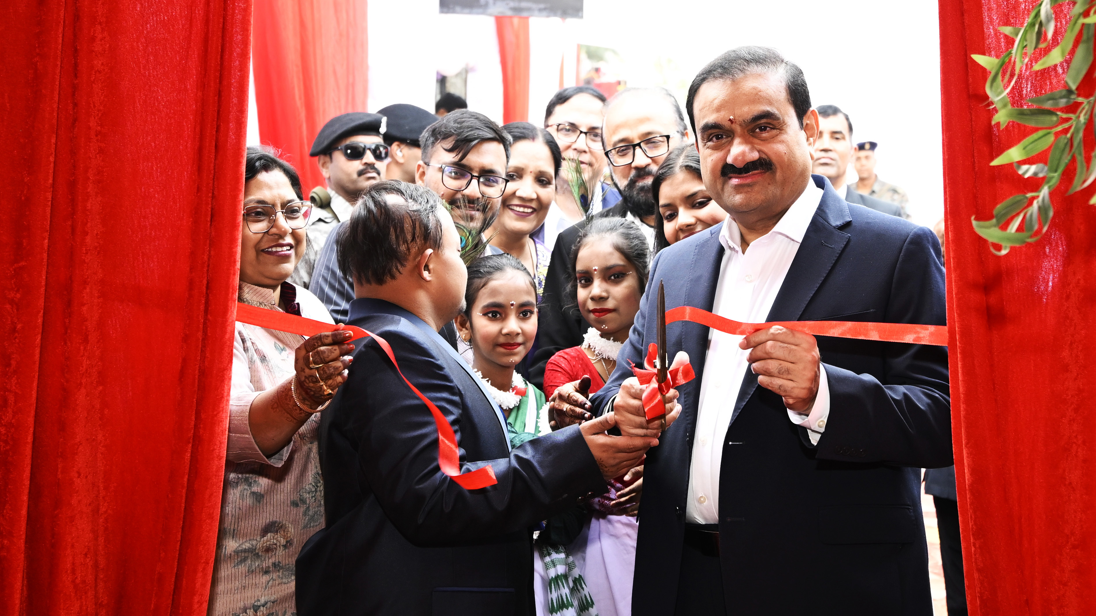 Gautam Adani cuts red ribbon, surrounded by smiling adults and children.