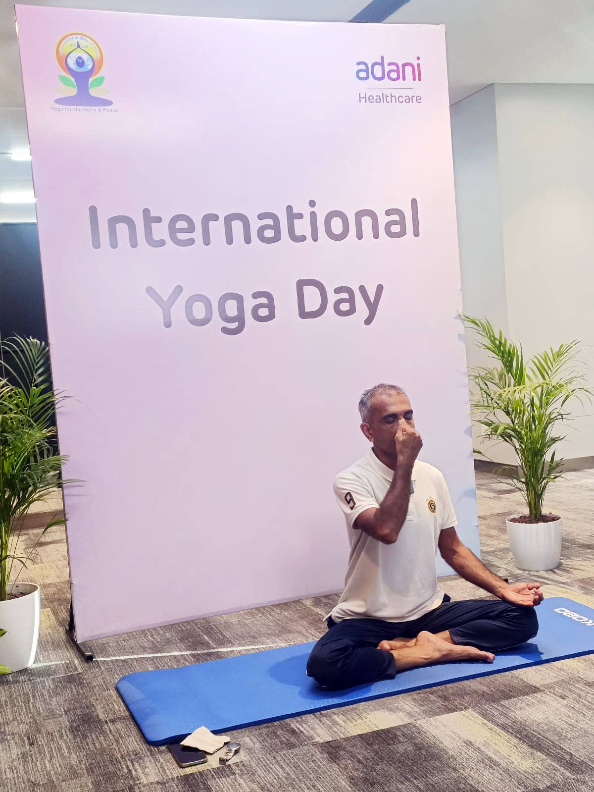 Man practicing yoga for International Yoga Day, with "Adani Healthcare" banner in the background.