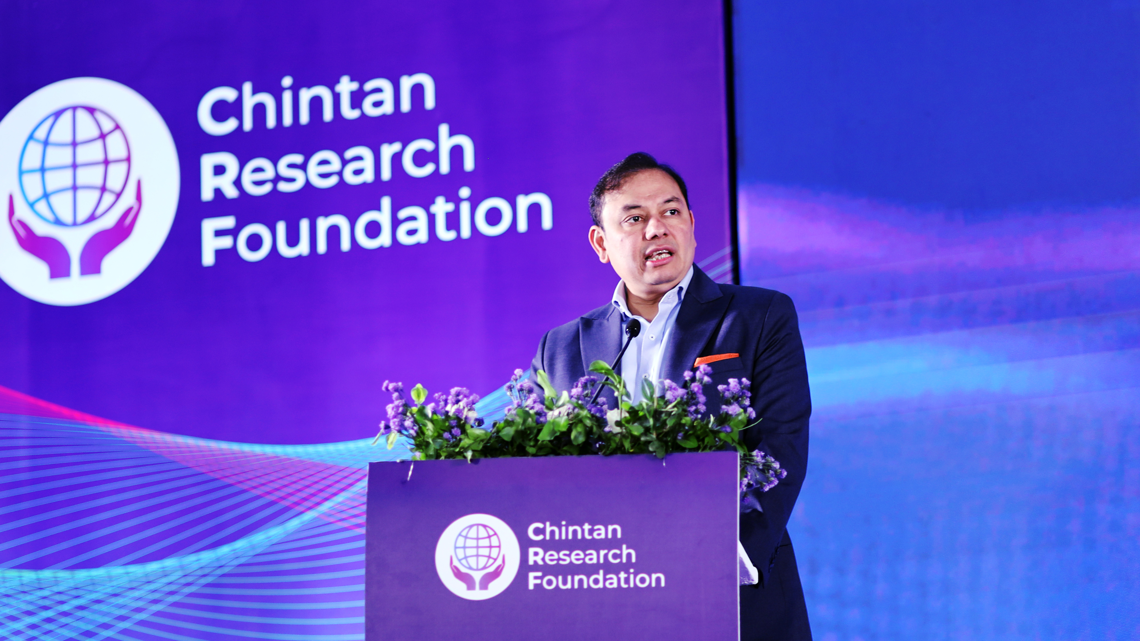 A man in a suit speaks at a podium with the 'Chintan Research Foundation' logo and text visible.