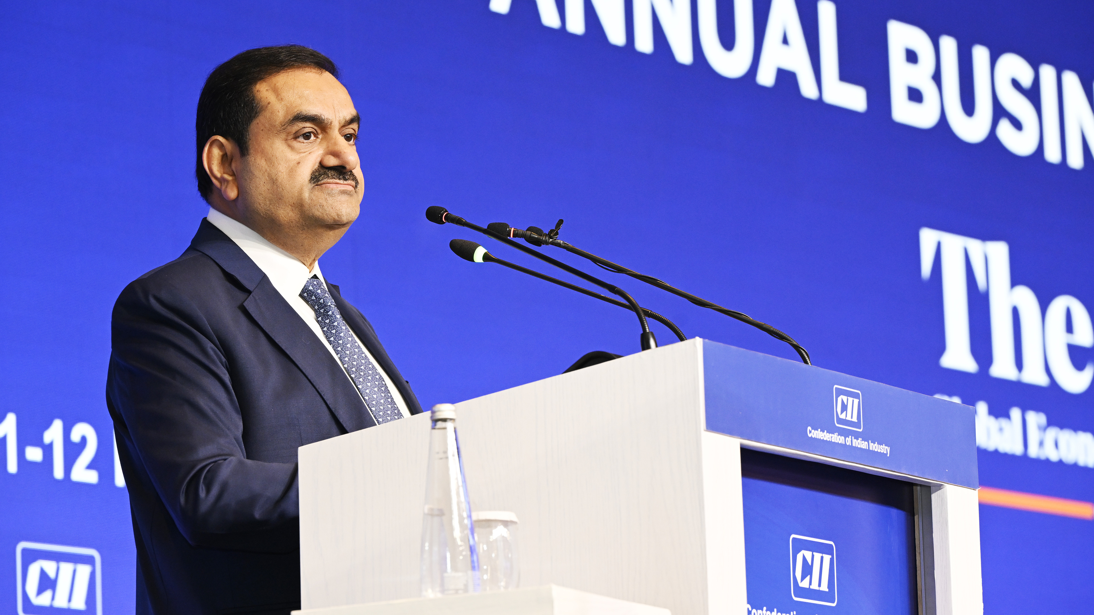 Gautam Adani, a prominent Indian businessman, speaking at a conference podium with microphones.