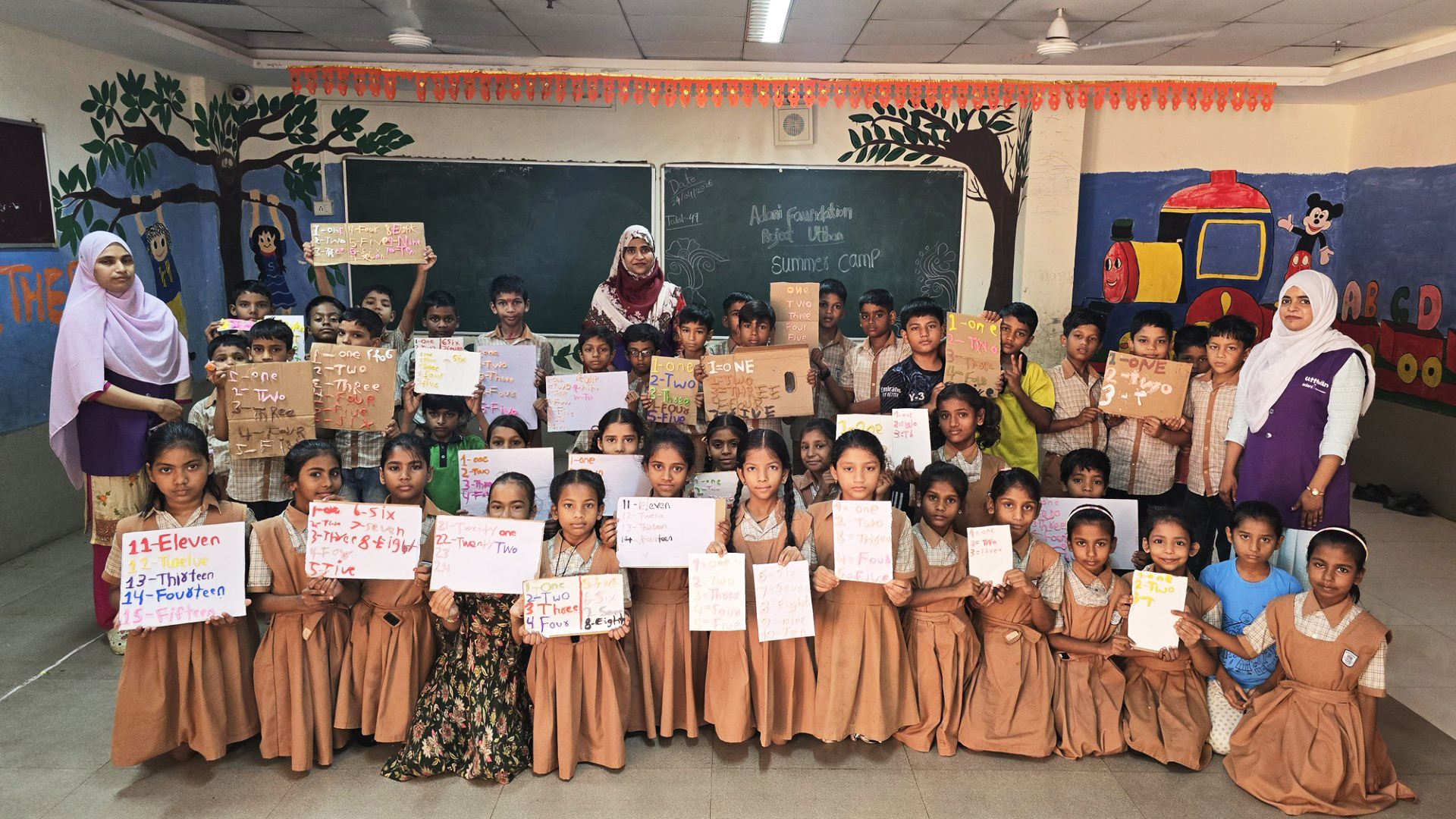Children and teachers at a summer camp display handmade number cards, indicating a learning activity.