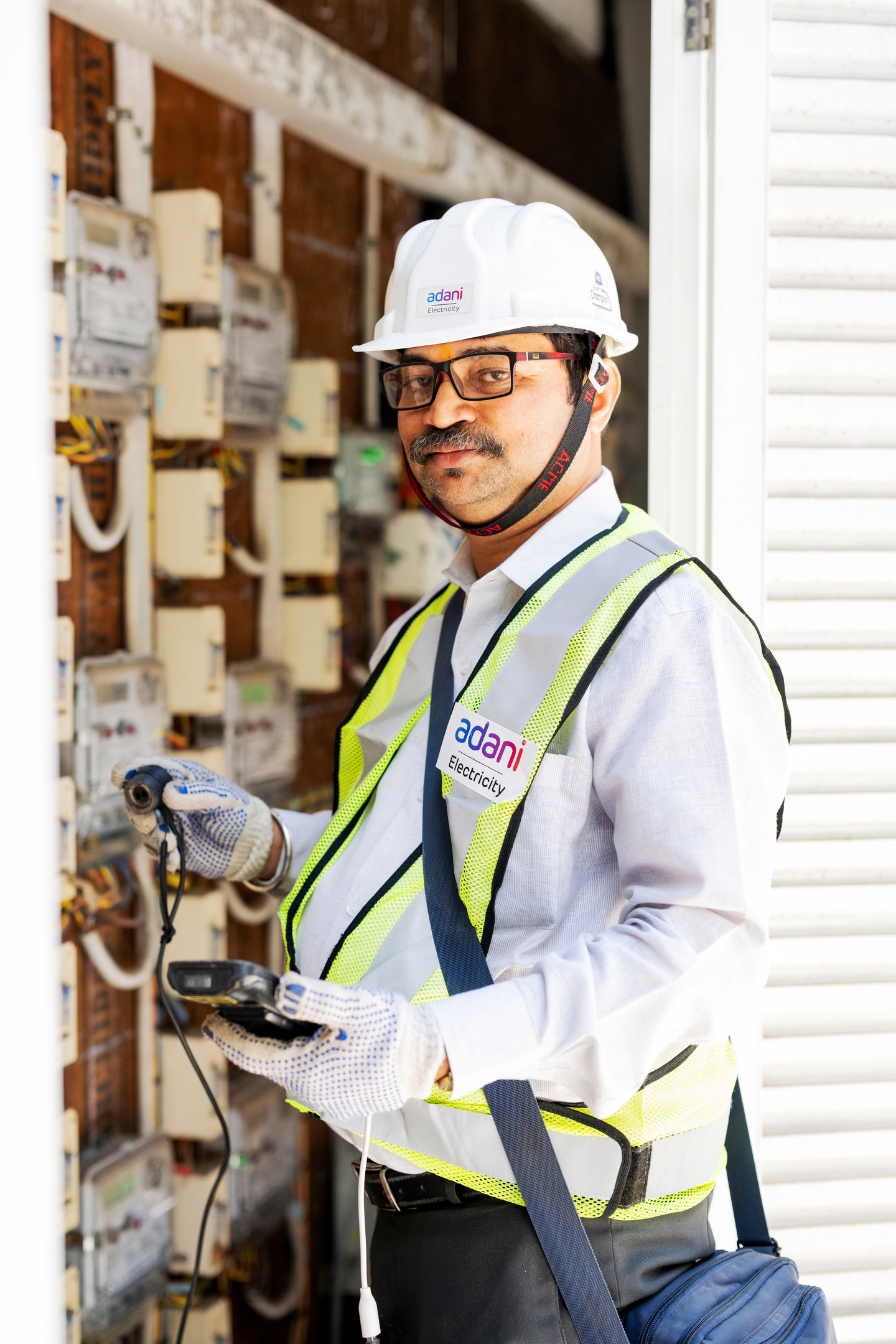 An Adani Electricity worker in a hard hat and safety vest checks electricity meters with a handheld device.