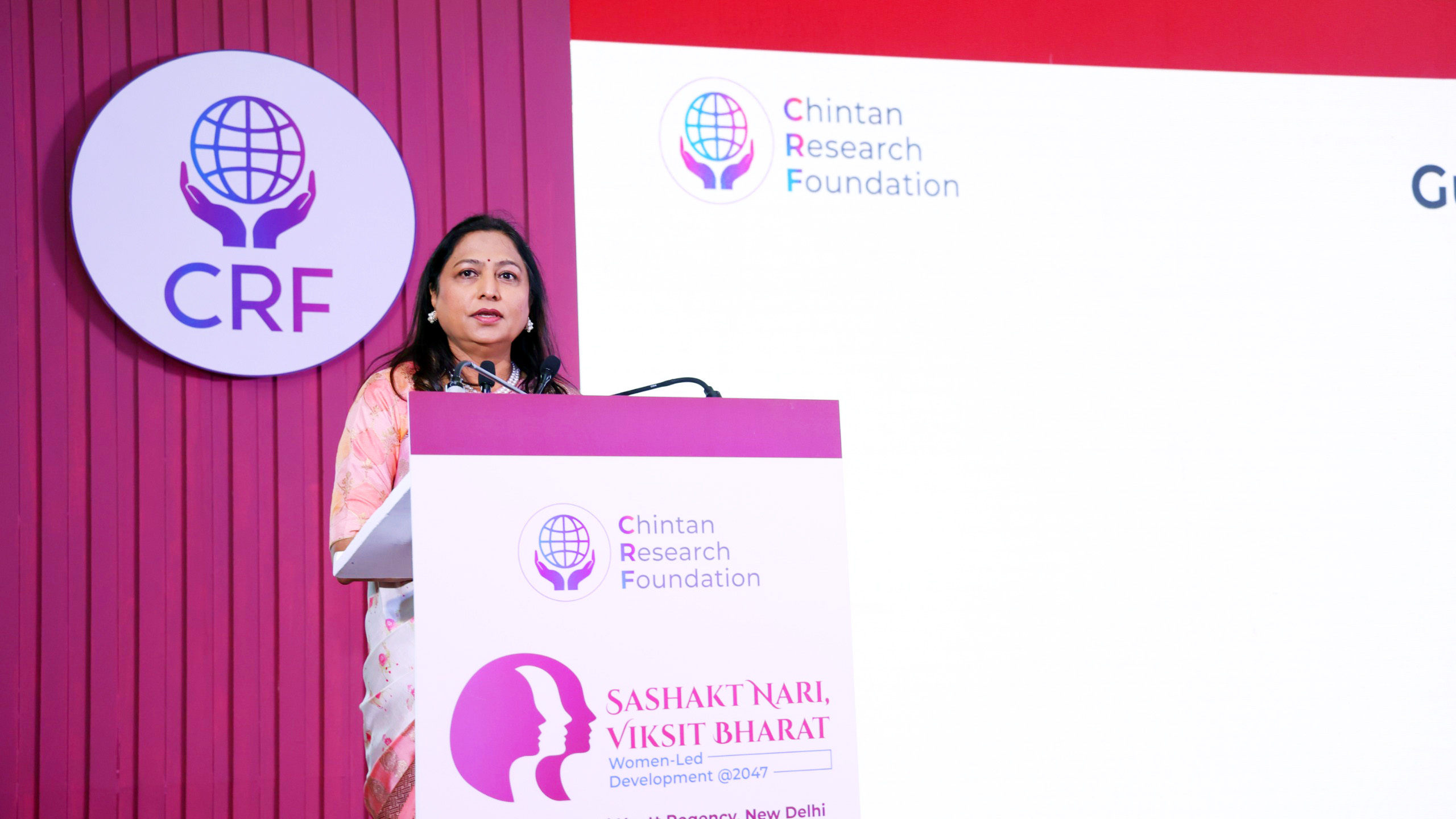 Woman speaking at a podium with CRF Chintan Research Foundation logo and 'SASHAKT NARI, VIKSIT BHARAT' text.