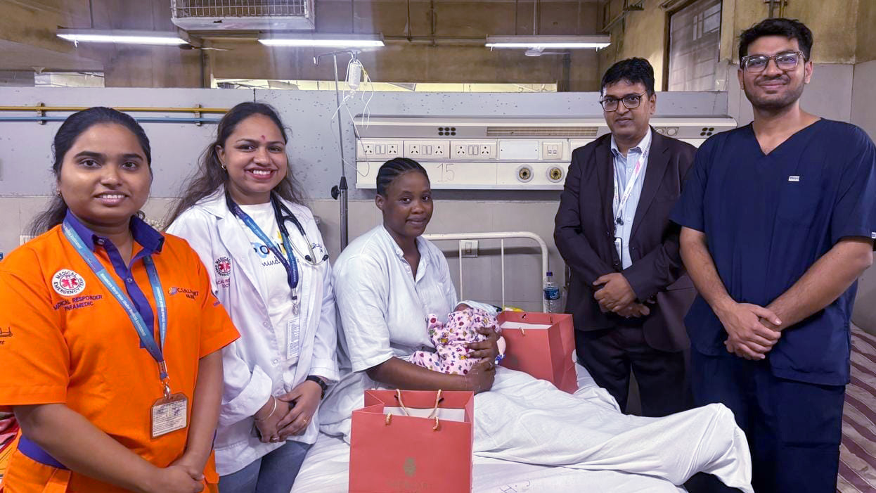 A new mother with her baby receives gifts from medical staff and administrators in a hospital room.