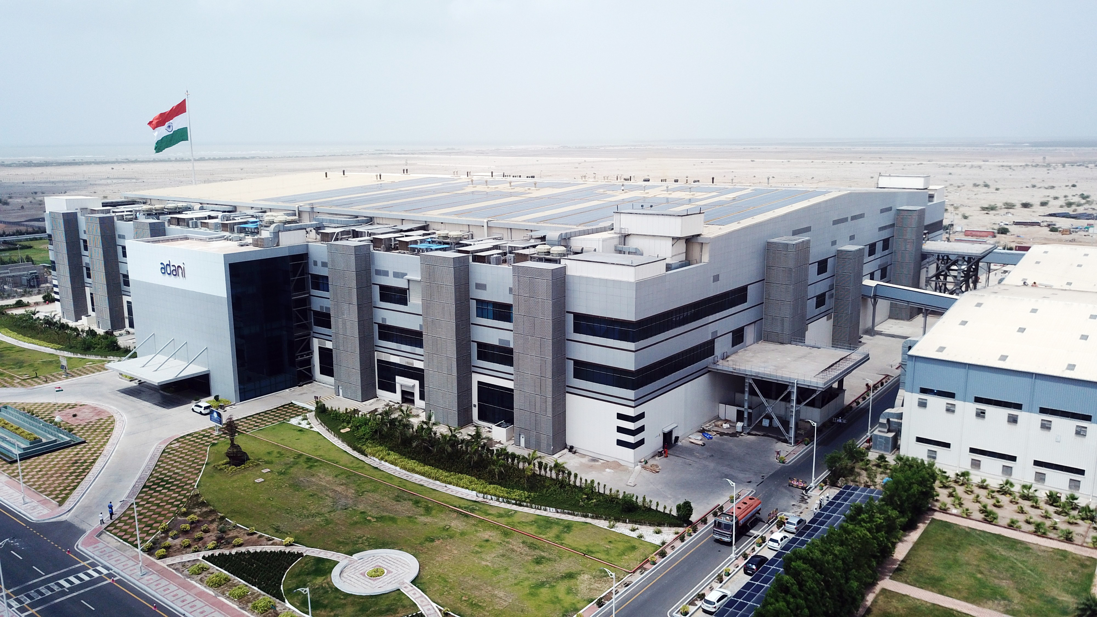 Aerial view of a modern Adani industrial complex featuring an Indian flag and rooftop solar panels.