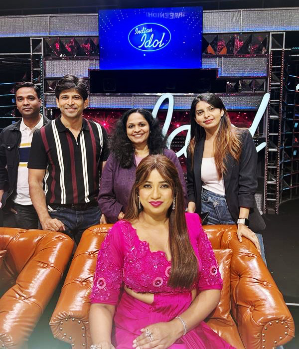 Five people, including singer Shreya Ghoshal in a pink outfit, pose on the Indian Idol set.