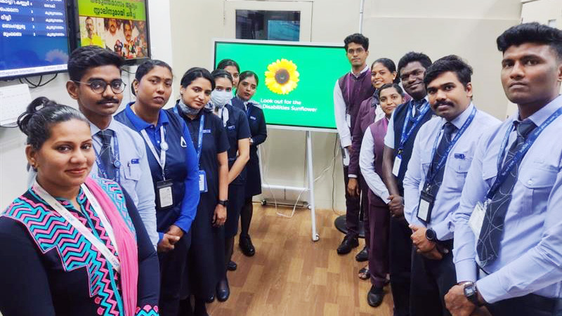 Airport staff in uniform pose before a screen showing the "Disabilities Sunflower" symbol.