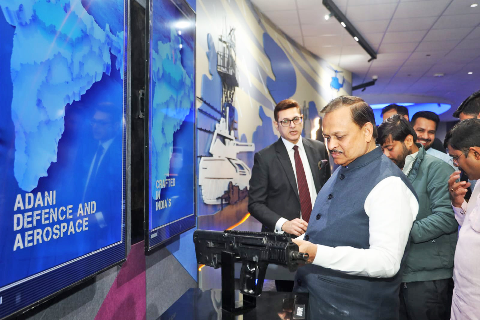 Man in a vest inspects a weapon at an Adani Defence and Aerospace exhibition.