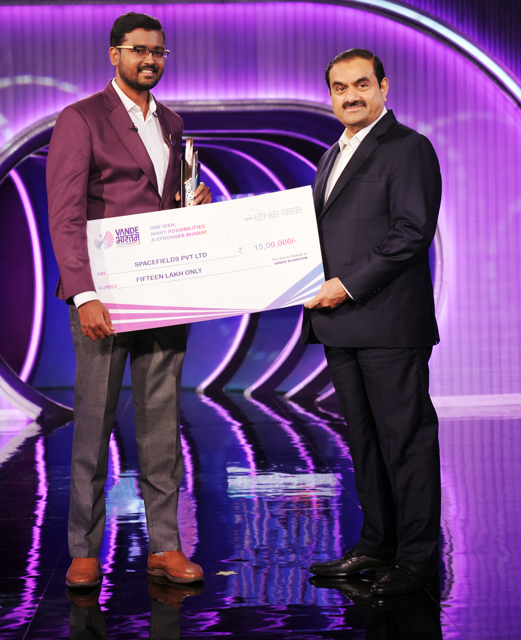 Two men, one holding a trophy, present a large check for 15 lakh to Spacefields Pvt Ltd.