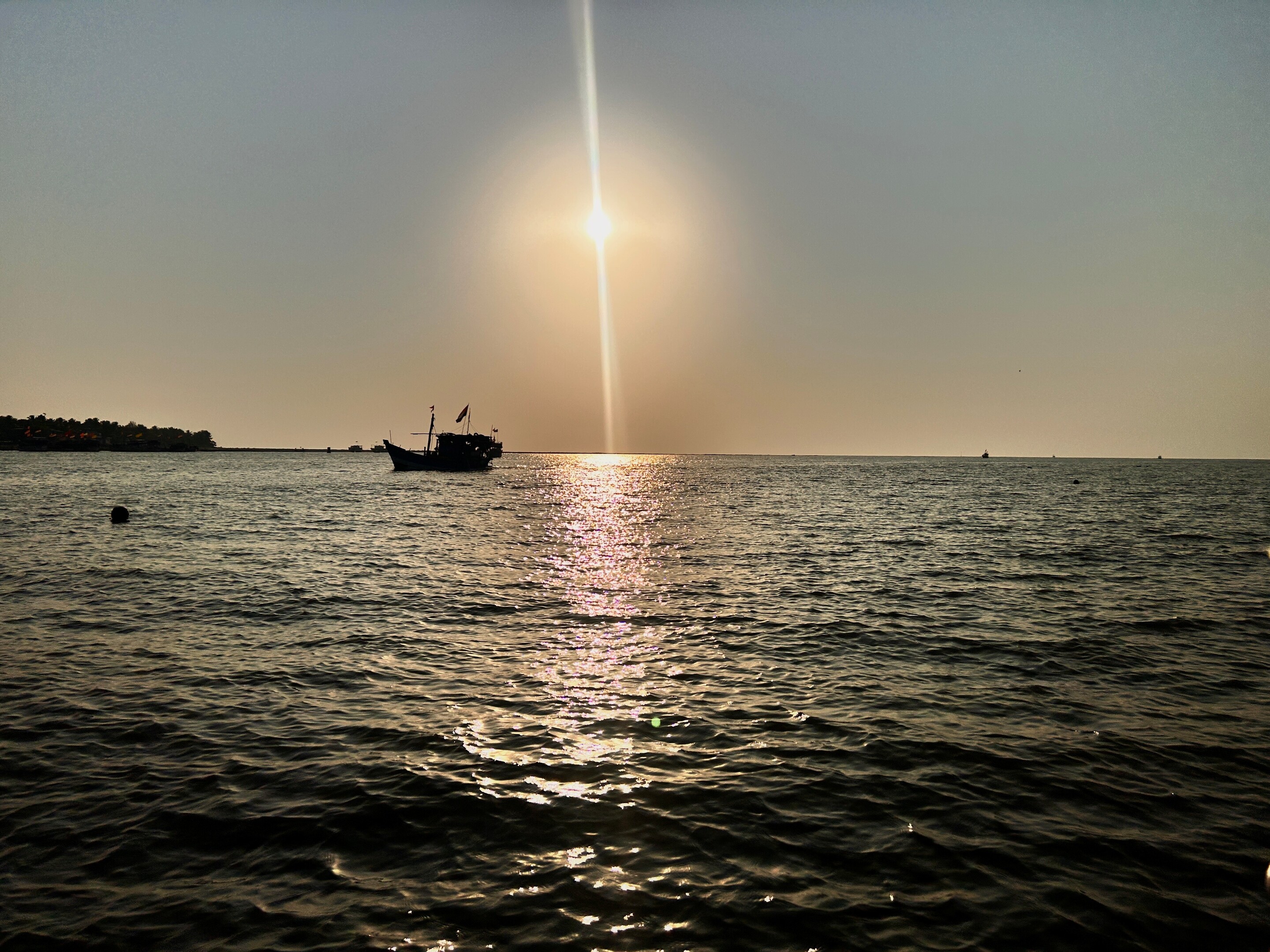 A silhouette of a fishing boat on the sea at sunset, with bright sun glare reflecting on the water.