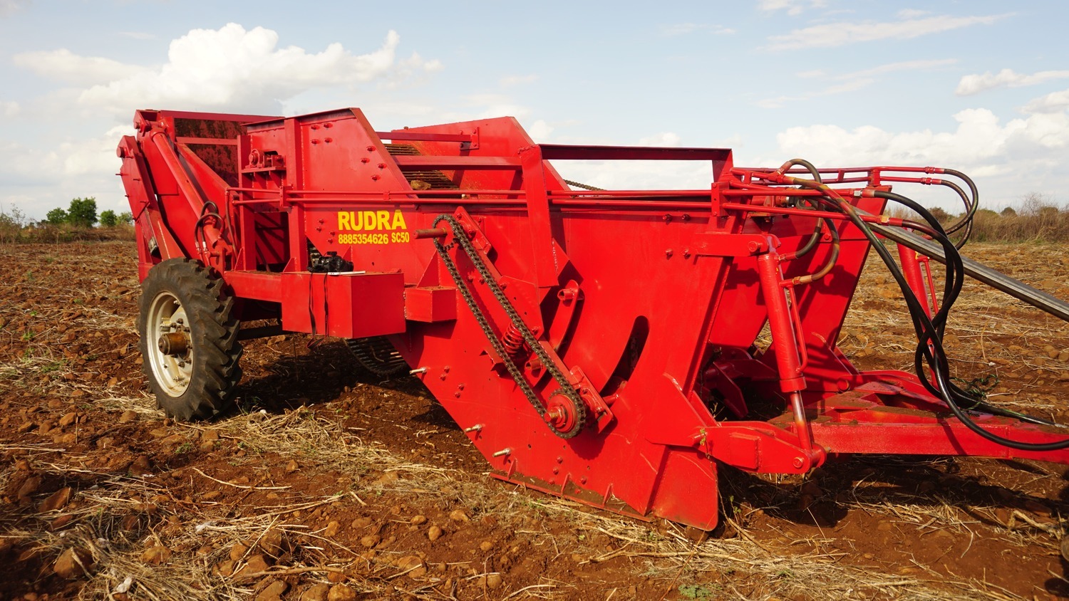 Red Rudra SC50 farm machinery, likely a potato harvester, standing in a tilled agricultural field under a cloudy sky.
