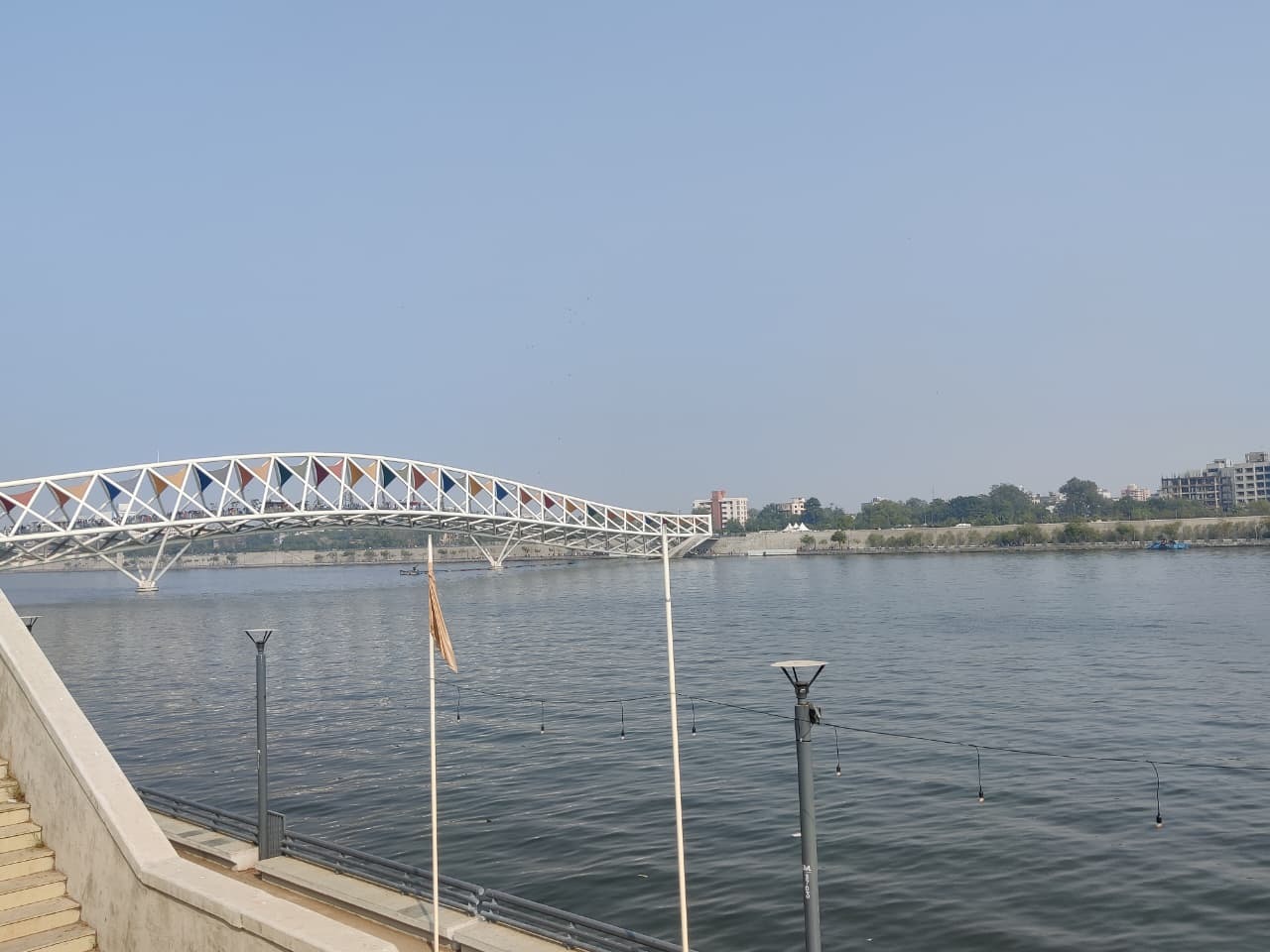 A colorful pedestrian bridge over a river, with city buildings and a promenade on a clear day.