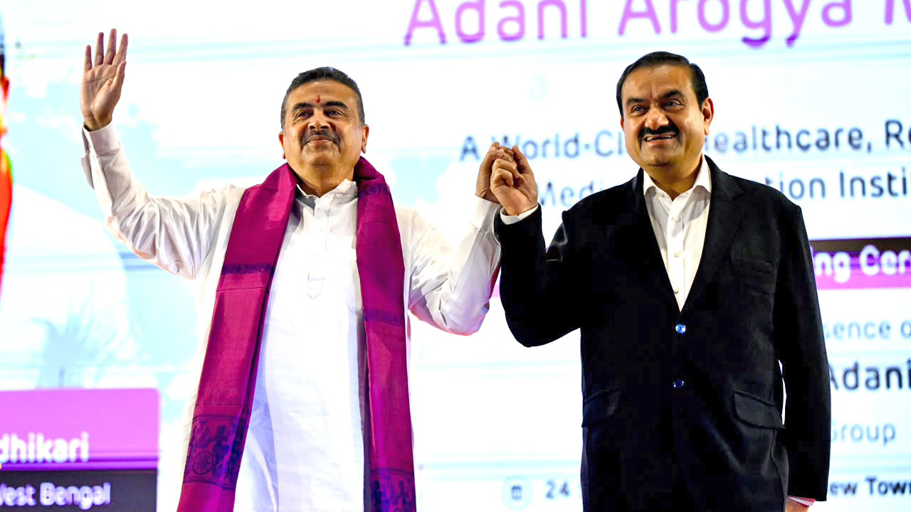 Indian billionaire Gautam Adani and politician Suvendu Adhikari smiling and holding hands at an event.