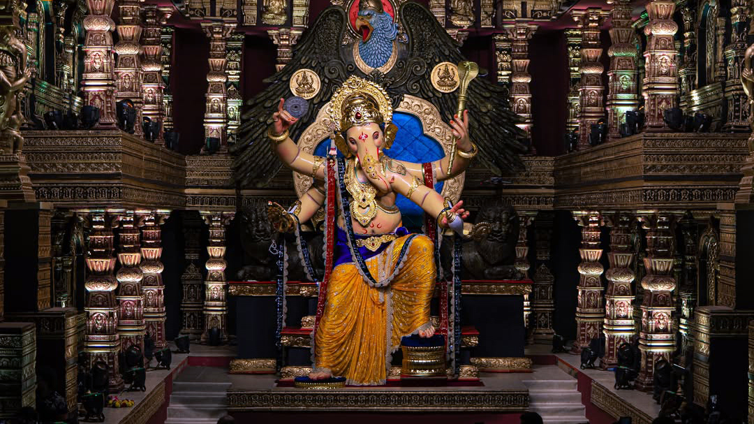 Elaborate golden Ganesha idol seated on a throne in a grand, ornately carved temple setting.