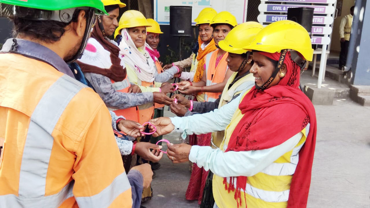 Construction workers in hard hats and vests exchange pink heart-shaped objects.