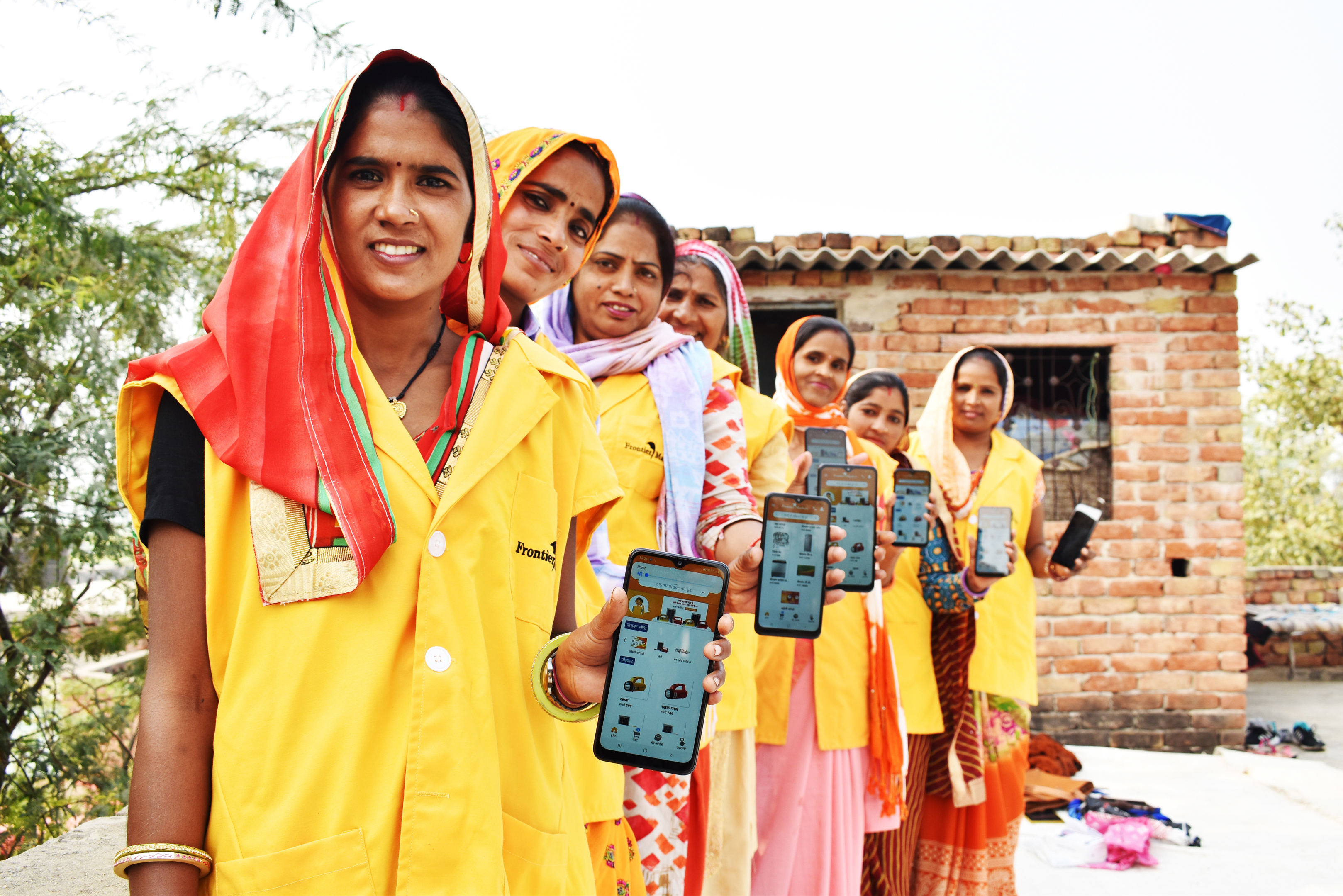 Rural women in yellow uniforms holding smartphones with an app, smiling at the camera.