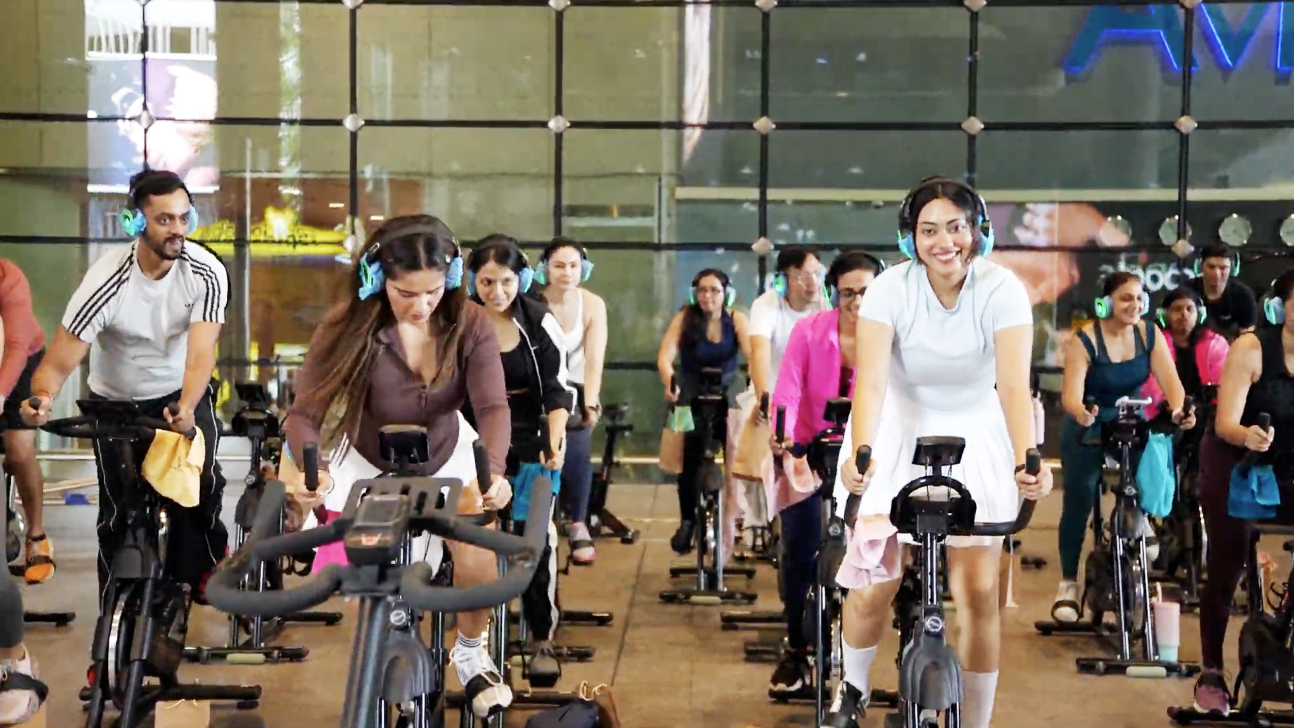 People wearing headphones on spin bikes in a fitness class, smiling and exercising indoors.