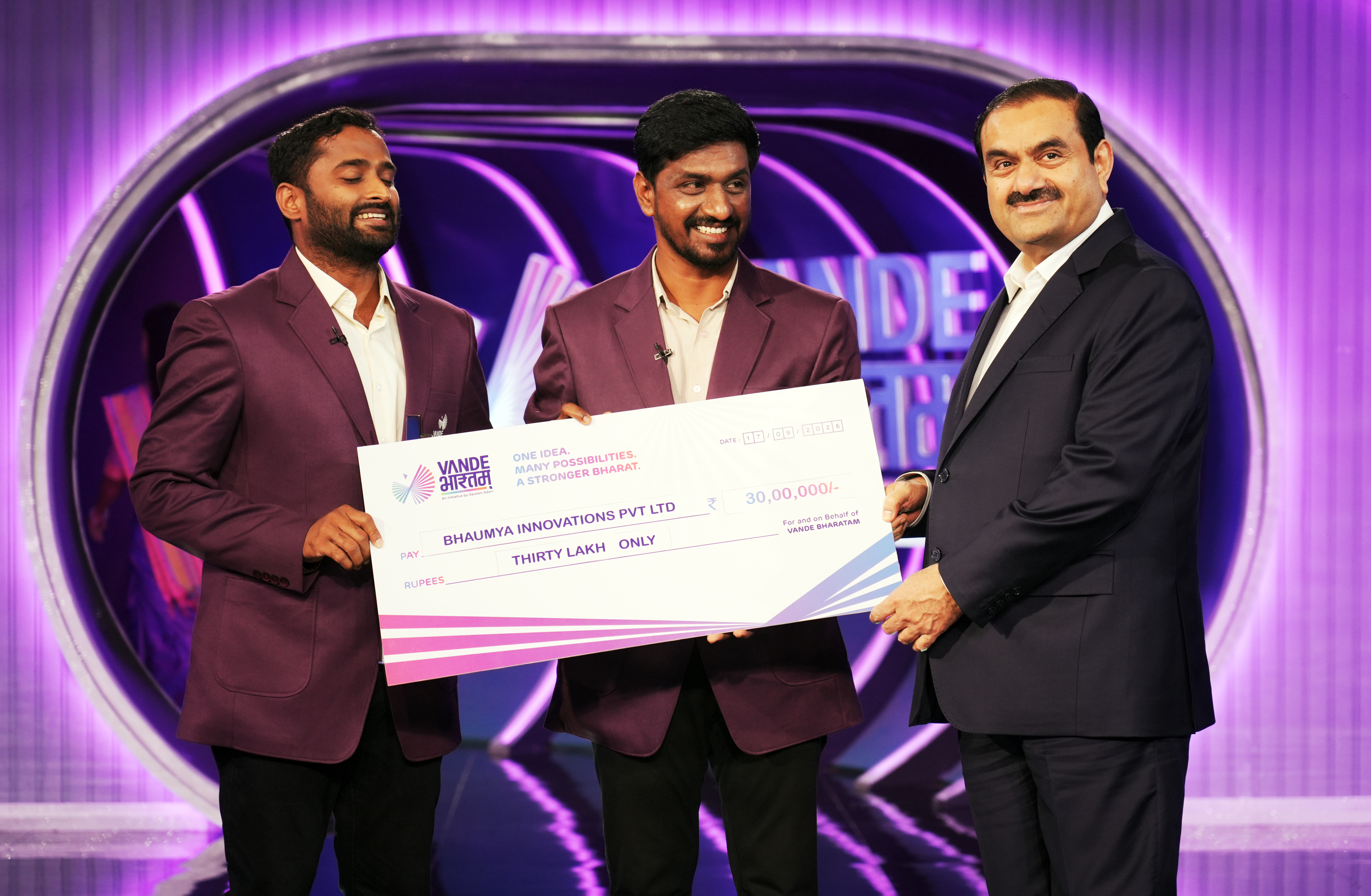 Gautam Adani and two men holding a large Vande Bharatam check for thirty lakh rupees.