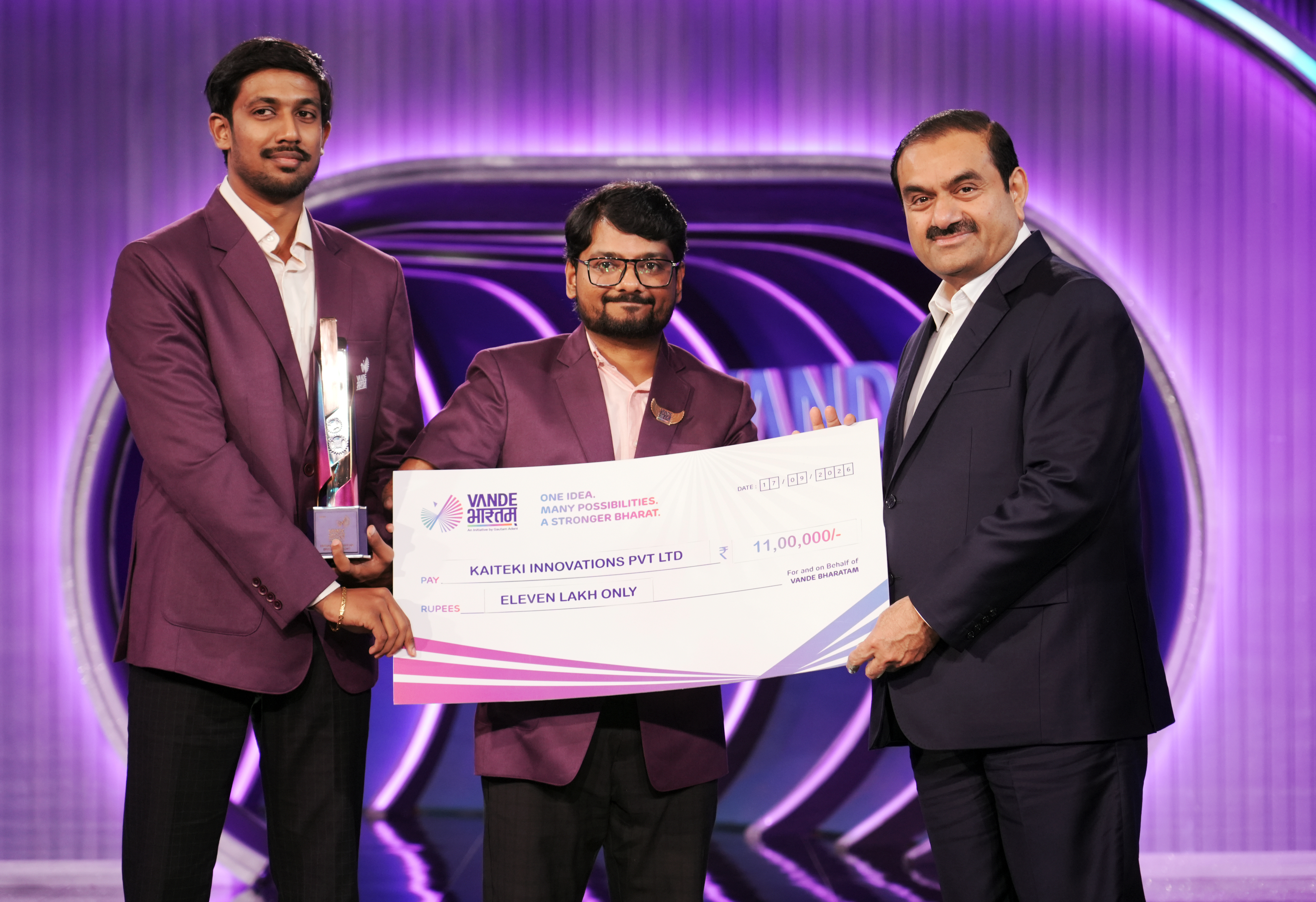 Three men, including Gautam Adani, pose with a large check for Eleven Lakh Only and a trophy.