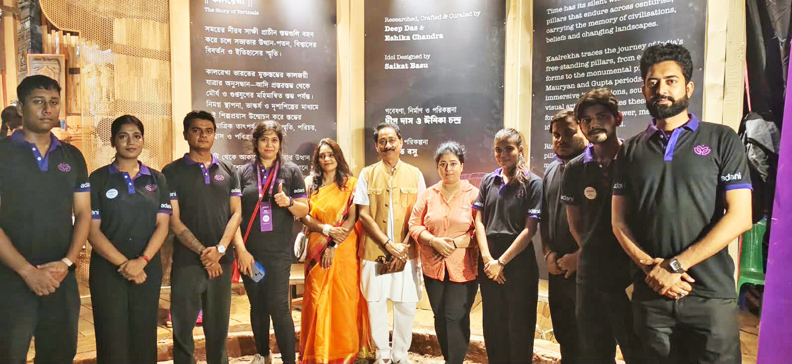 Group of people, some in Adani uniforms, posing in front of informational panels at an event.
