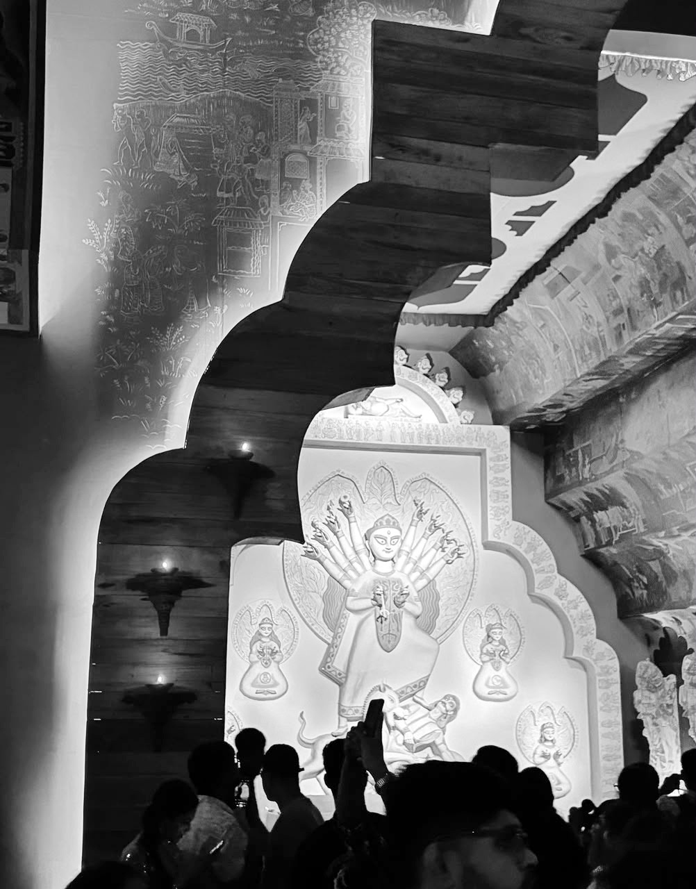Black and white photo of people in a crowd viewing a large, ornate Goddess Durga idol at a pandal.