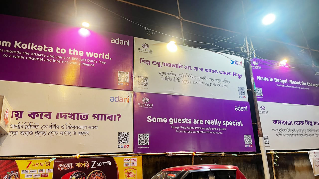 Multiple Adani billboards promoting Durga Puja, some in English, some in Bengali, lit up at night.