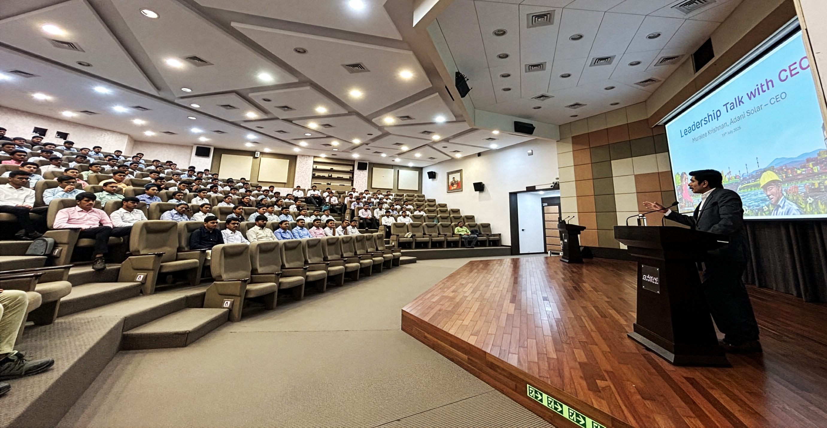 A speaker delivers a "Leadership Talk with CEO" to a large audience seated in a spacious auditorium.