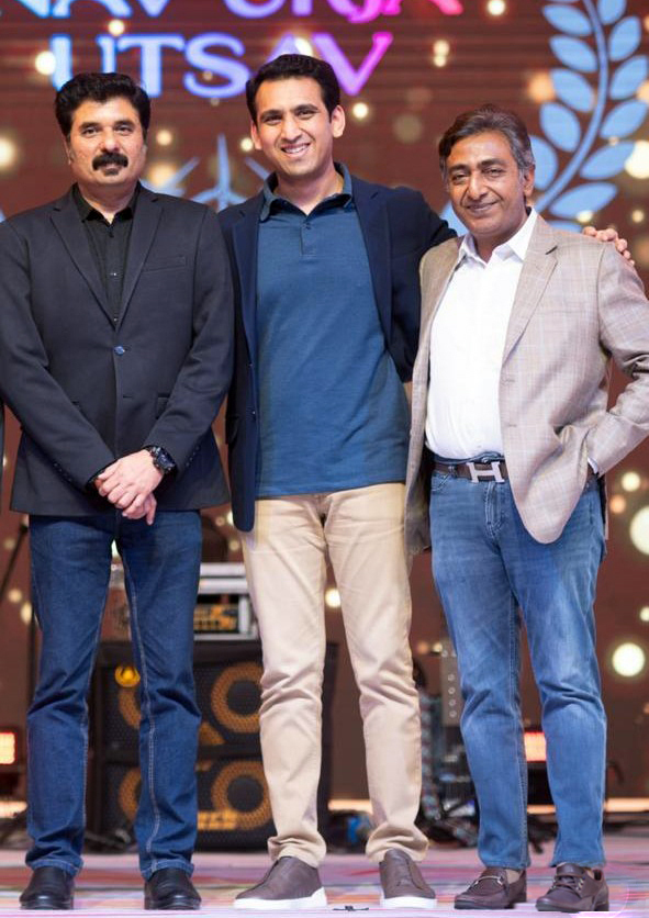 Three men stand on a stage, dressed in smart casual attire, smiling and posing for a photo.