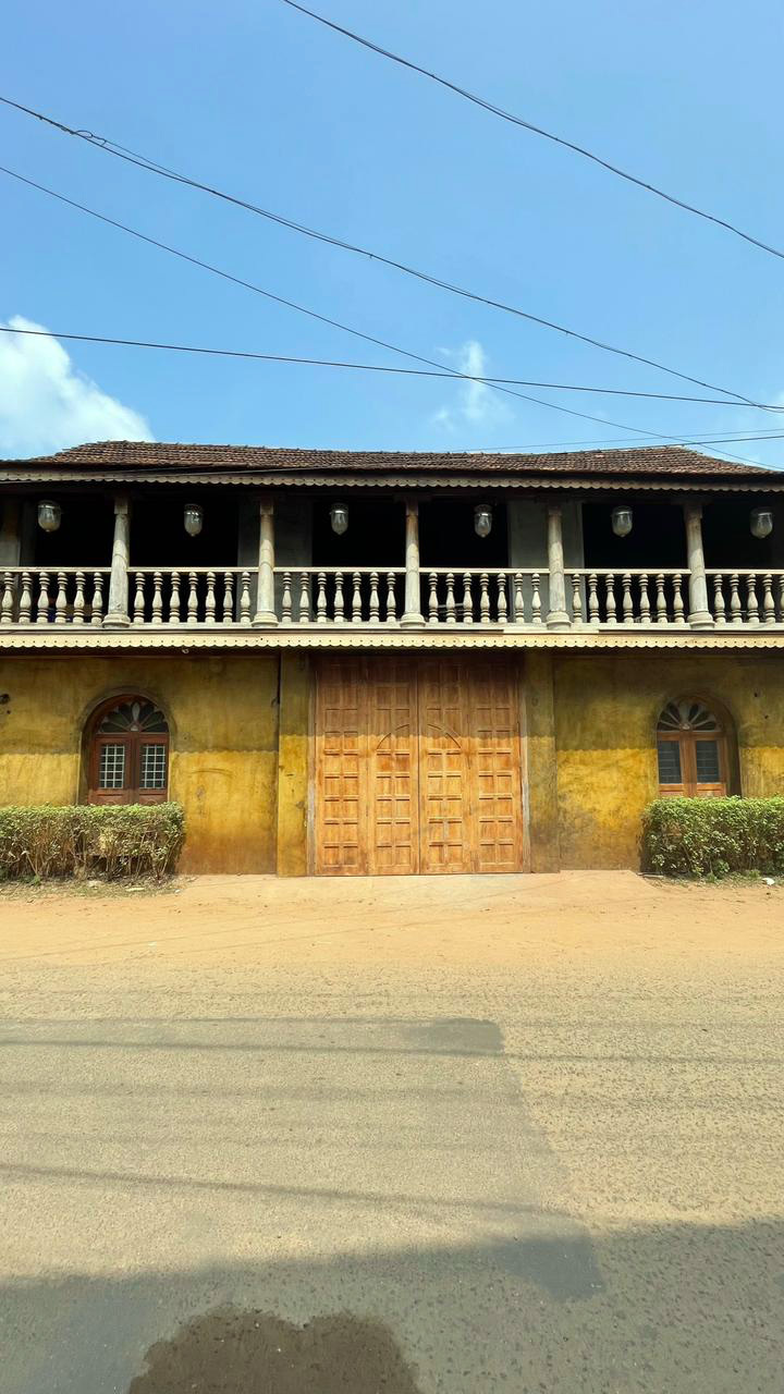 Traditional two-story building with yellow facade, large wooden gate, and a balcony with pillars under a blue sky.