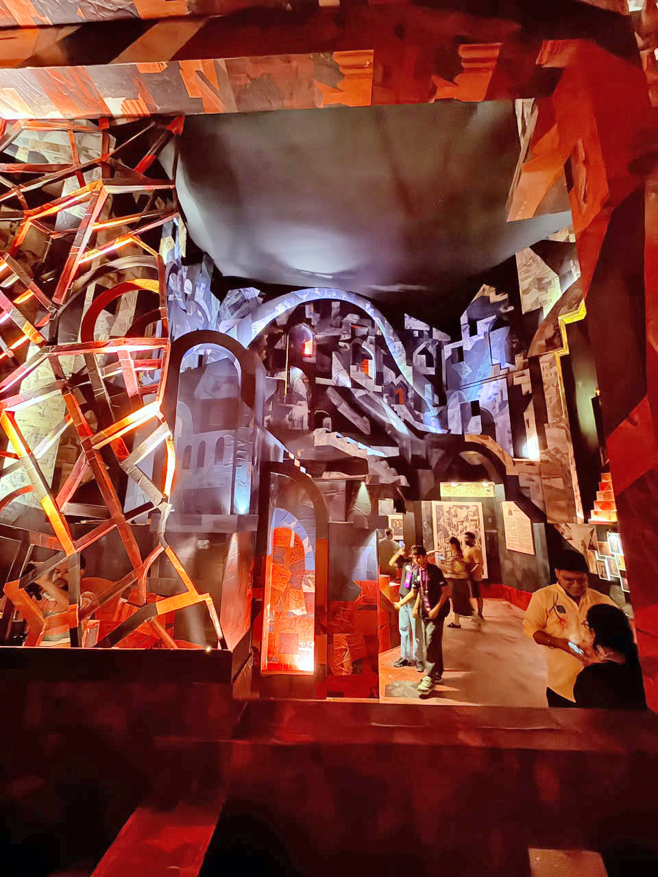 People explore an elaborate, abstract art installation or pandal with dramatic red and blue lighting.