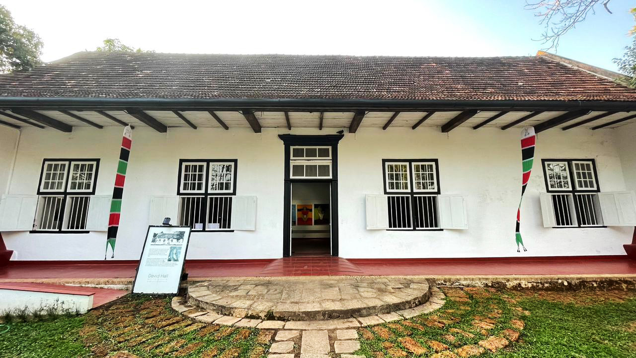 White colonial building with dark tiled roof, black-framed windows, central doorway, and colorful banners.