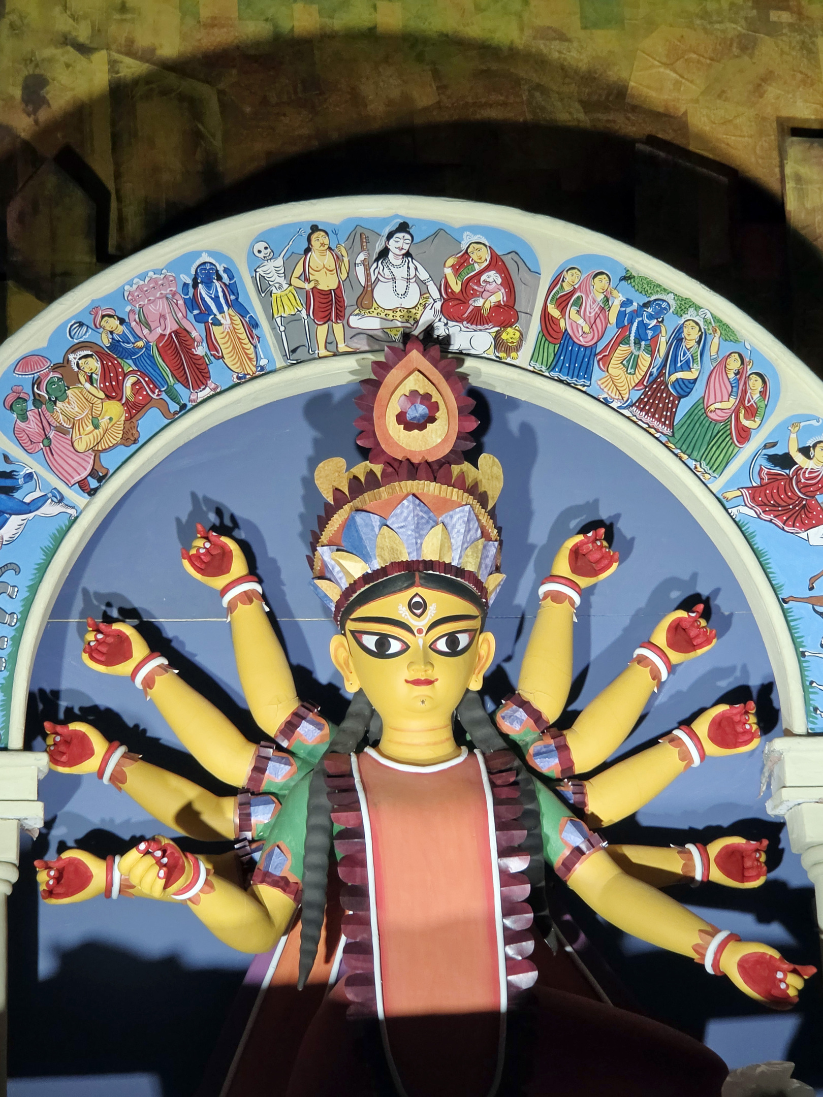 A vibrant, multi-armed Durga idol with a third eye, seated before a colorful painted arch.