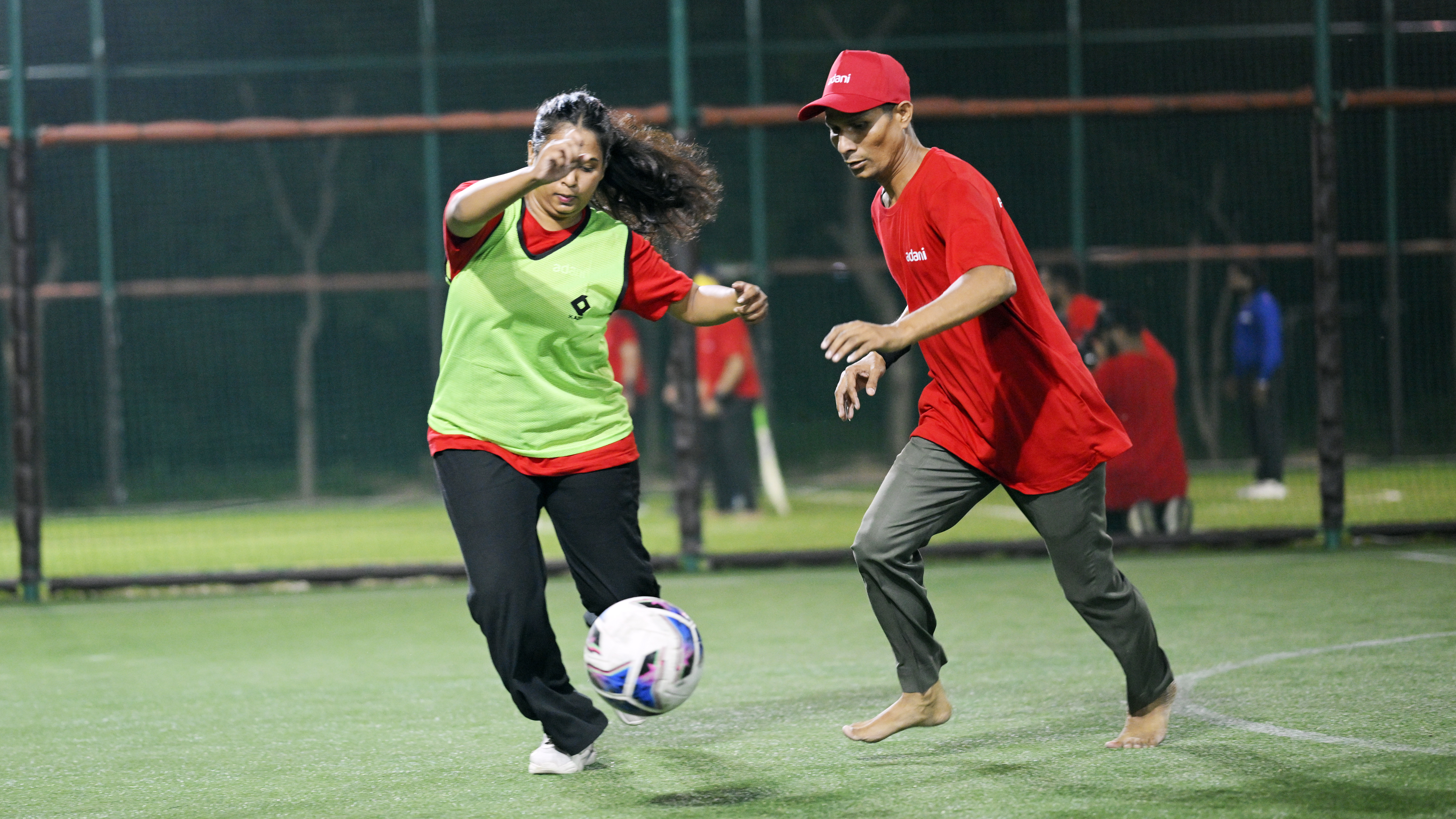 Two players, a woman and a man, engaged in a soccer game on a green turf field with a ball.