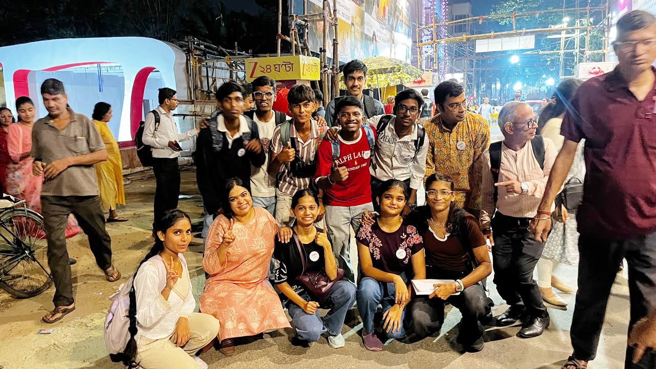 A large group of young people, some standing and some crouching, smiling for a photo at a night event.