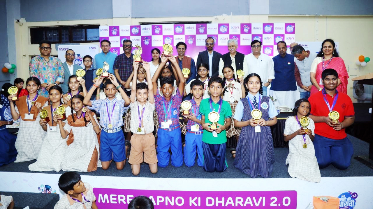 Children and adults pose with trophies and medals on a stage with "Adani Dharavi" branding.