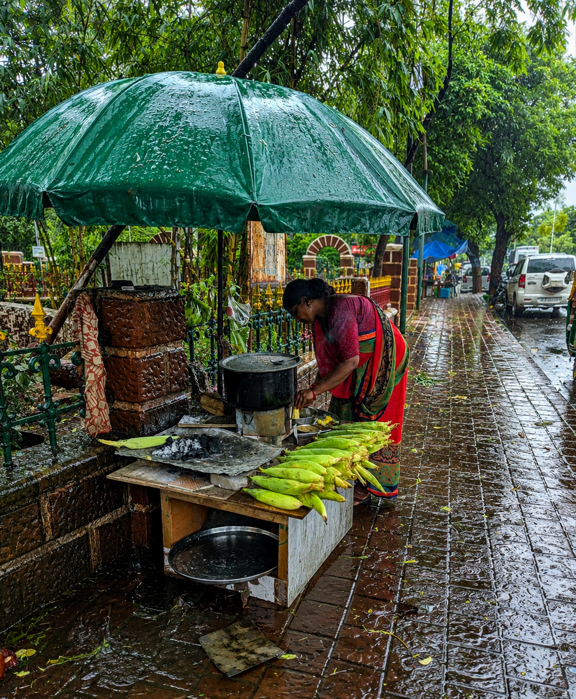 A woman under a green umbrella sells grilled corn on the cob from a street stall on a rainy day.