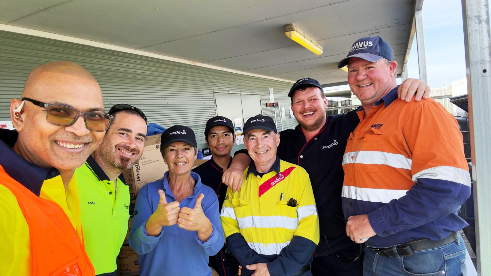 A group of seven smiling workers, some in uniform, posing together at an outdoor site.