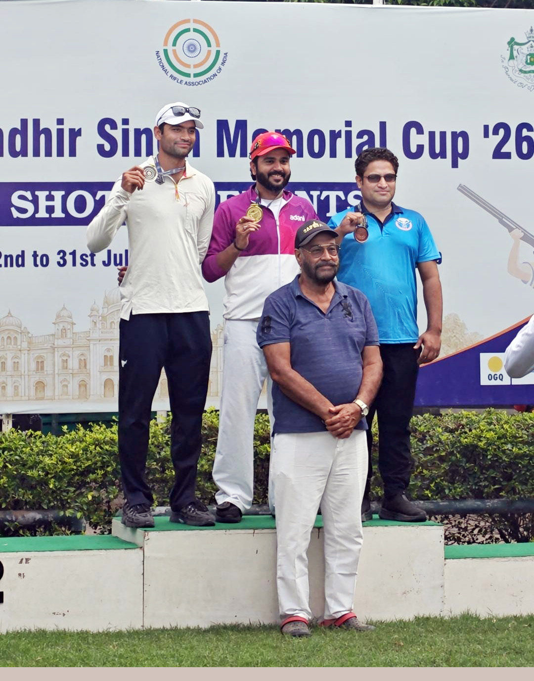 Four men, including medalists, stand on and in front of a podium at the Randhir Singh Memorial Cup.