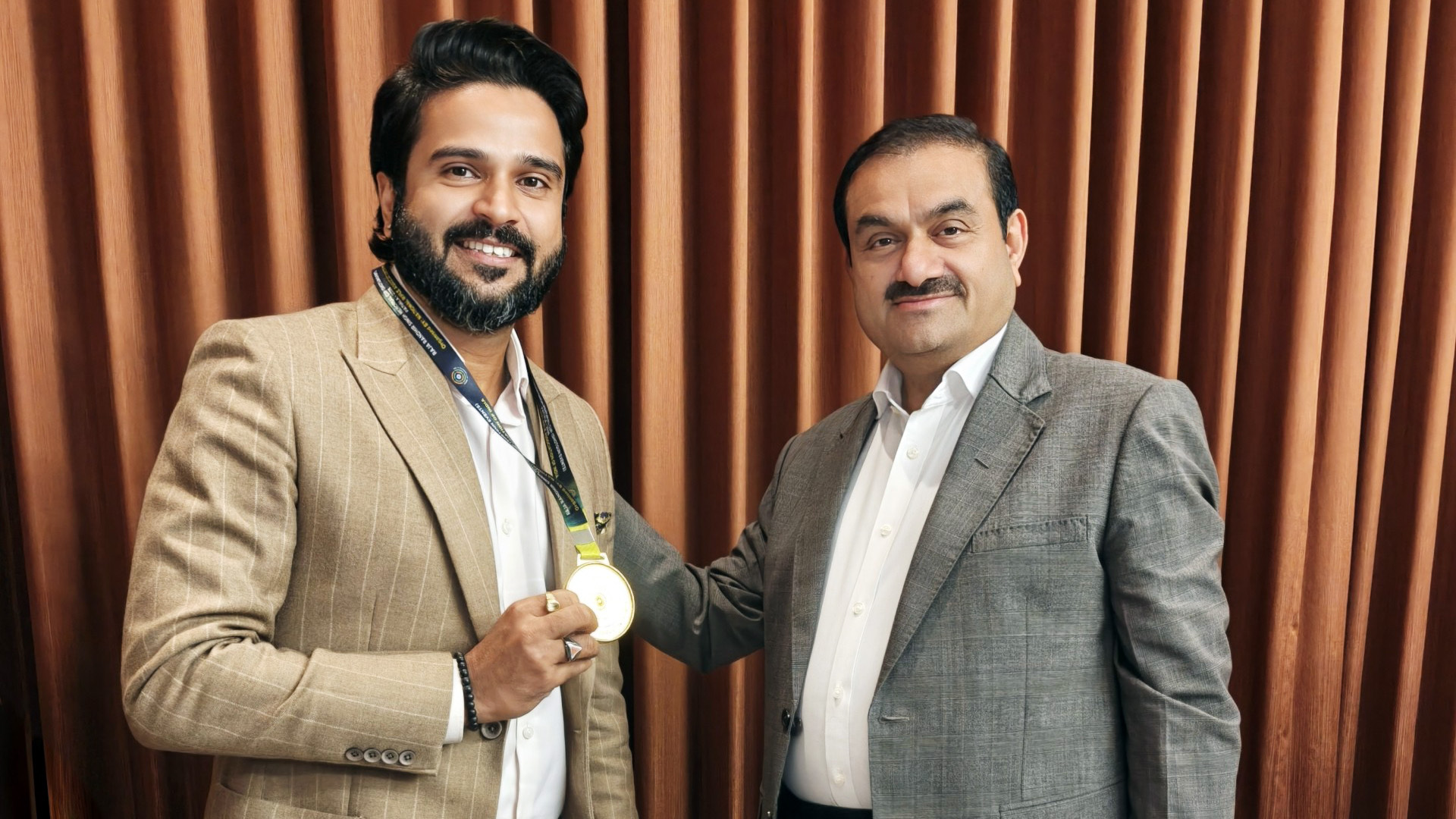 Two men, one holding a medal, standing side by side and smiling. Gautam Adani is on the right.