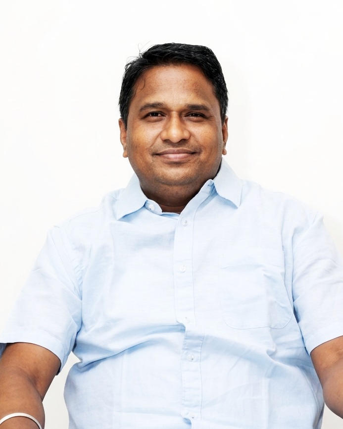 Portrait of a smiling South Asian man in a light blue collared shirt looking directly at the camera.