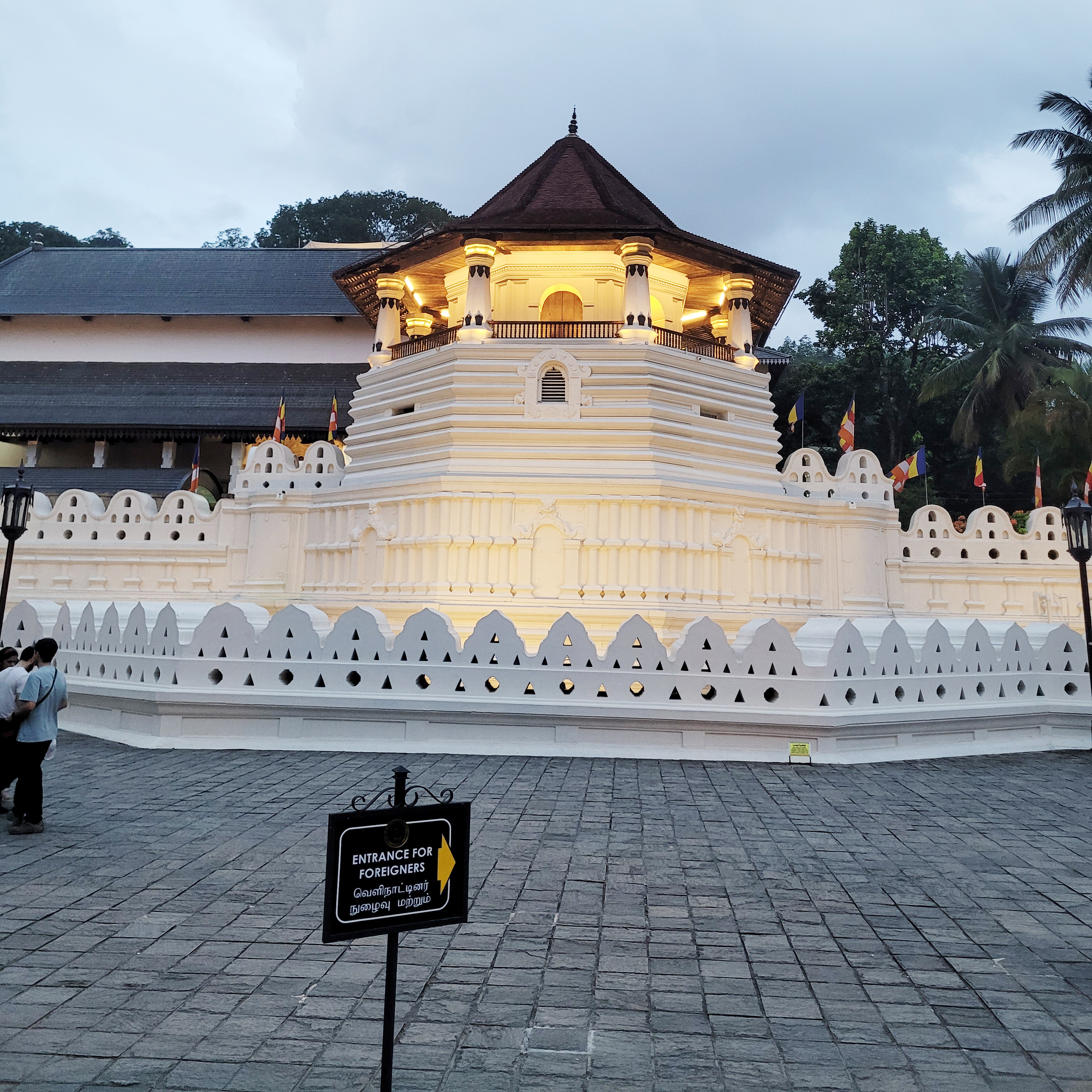 The illuminated Temple of the Sacred Tooth Relic at dusk, with an "Entrance for Foreigners" sign in the foreground.