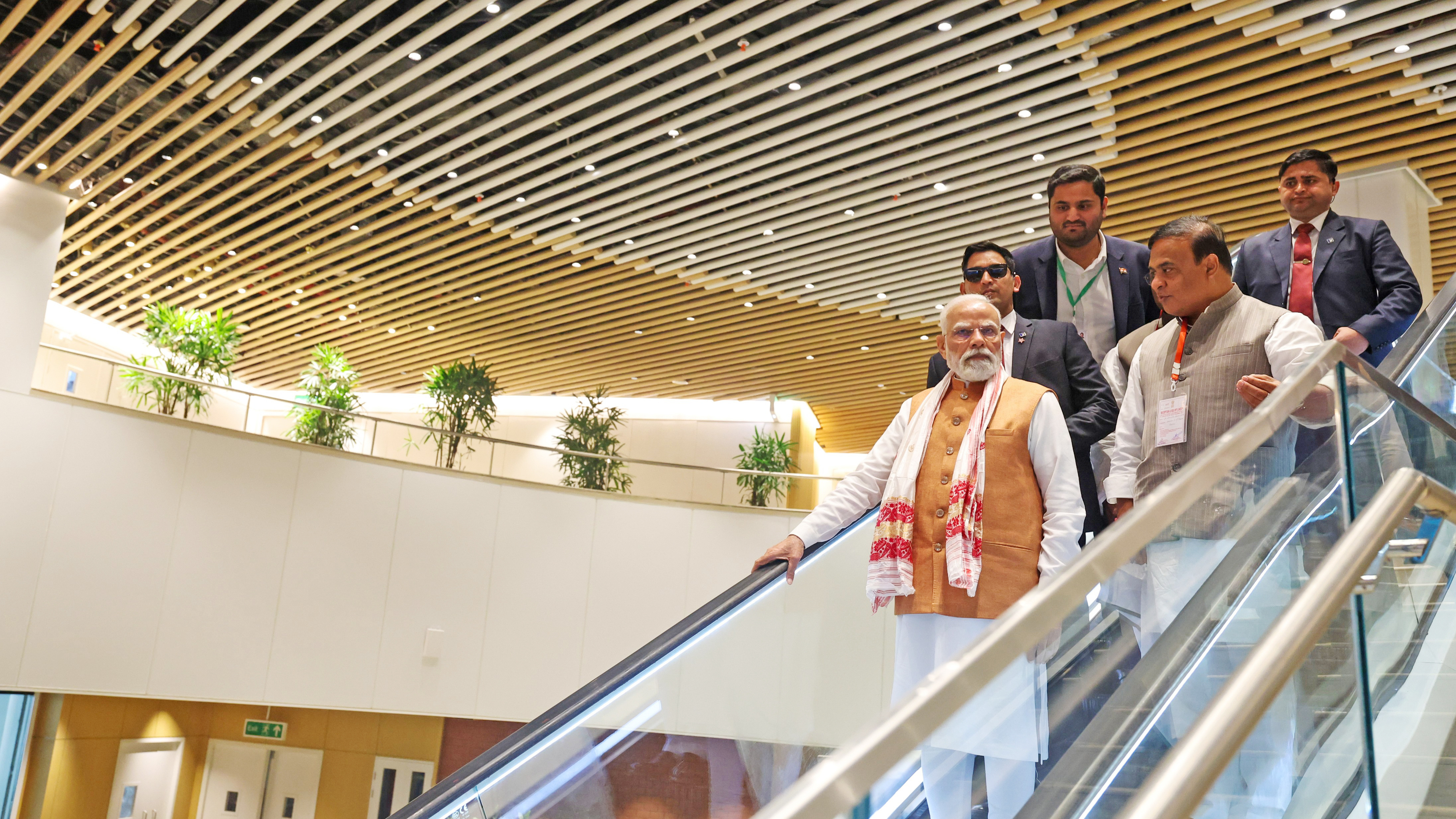 Narendra Modi in Indian attire descends an escalator with his entourage.