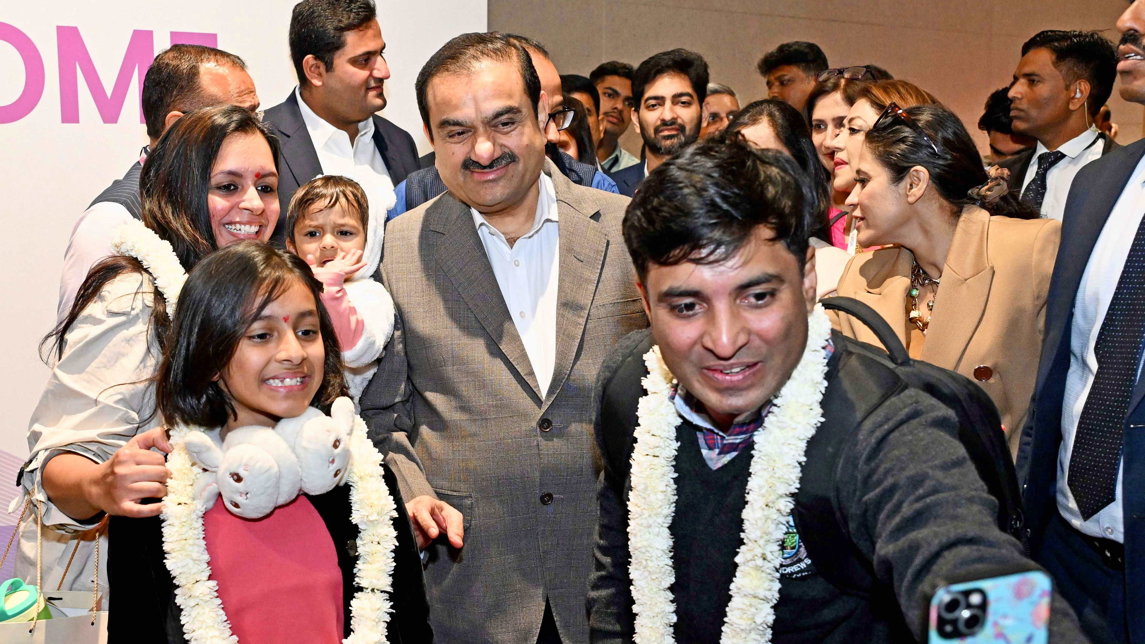Gautam Adani and a crowd, some wearing garlands, pose for a selfie.