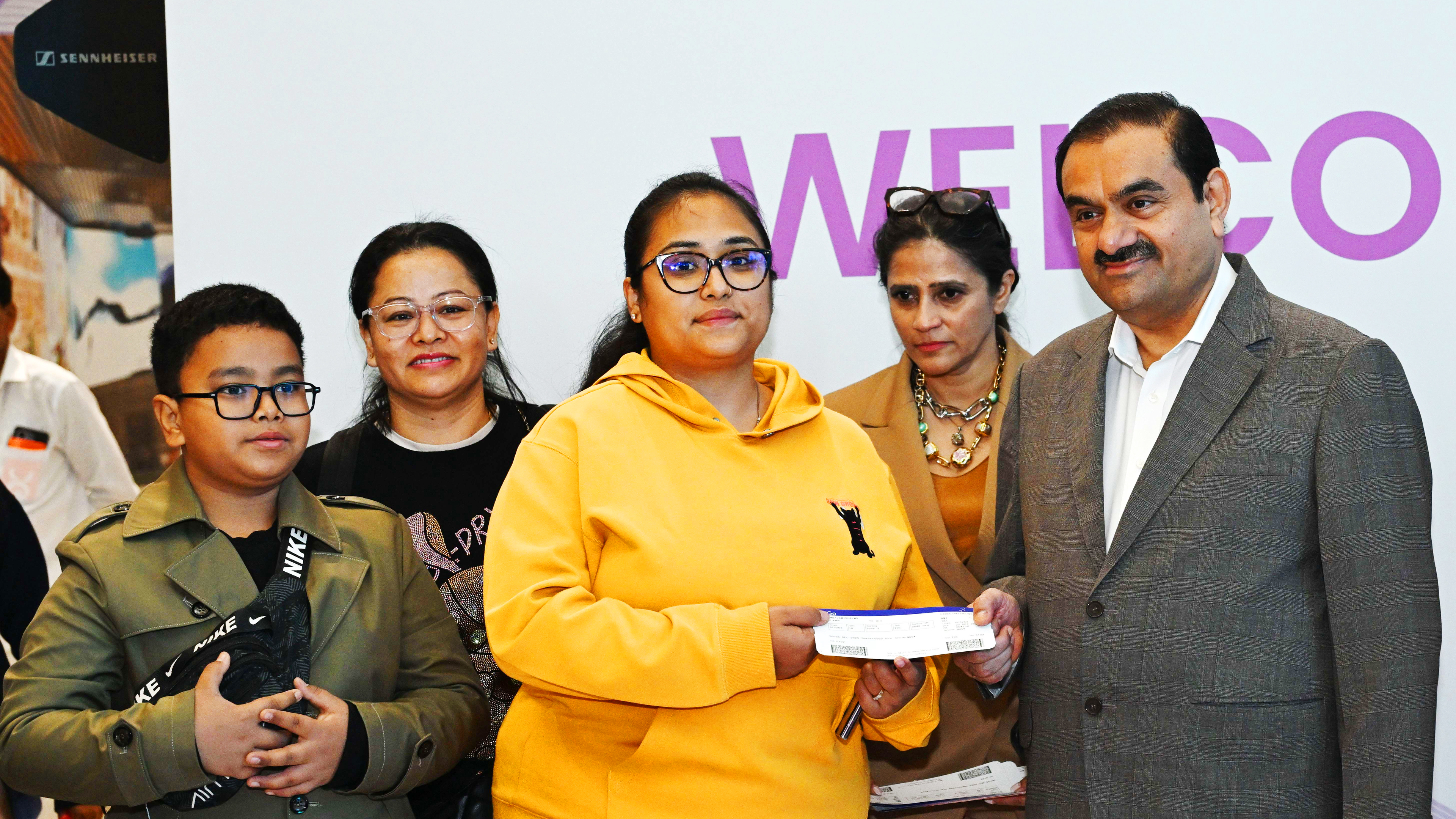 Gautam Adani and a woman with a family; a girl in a yellow hoodie holds tickets.