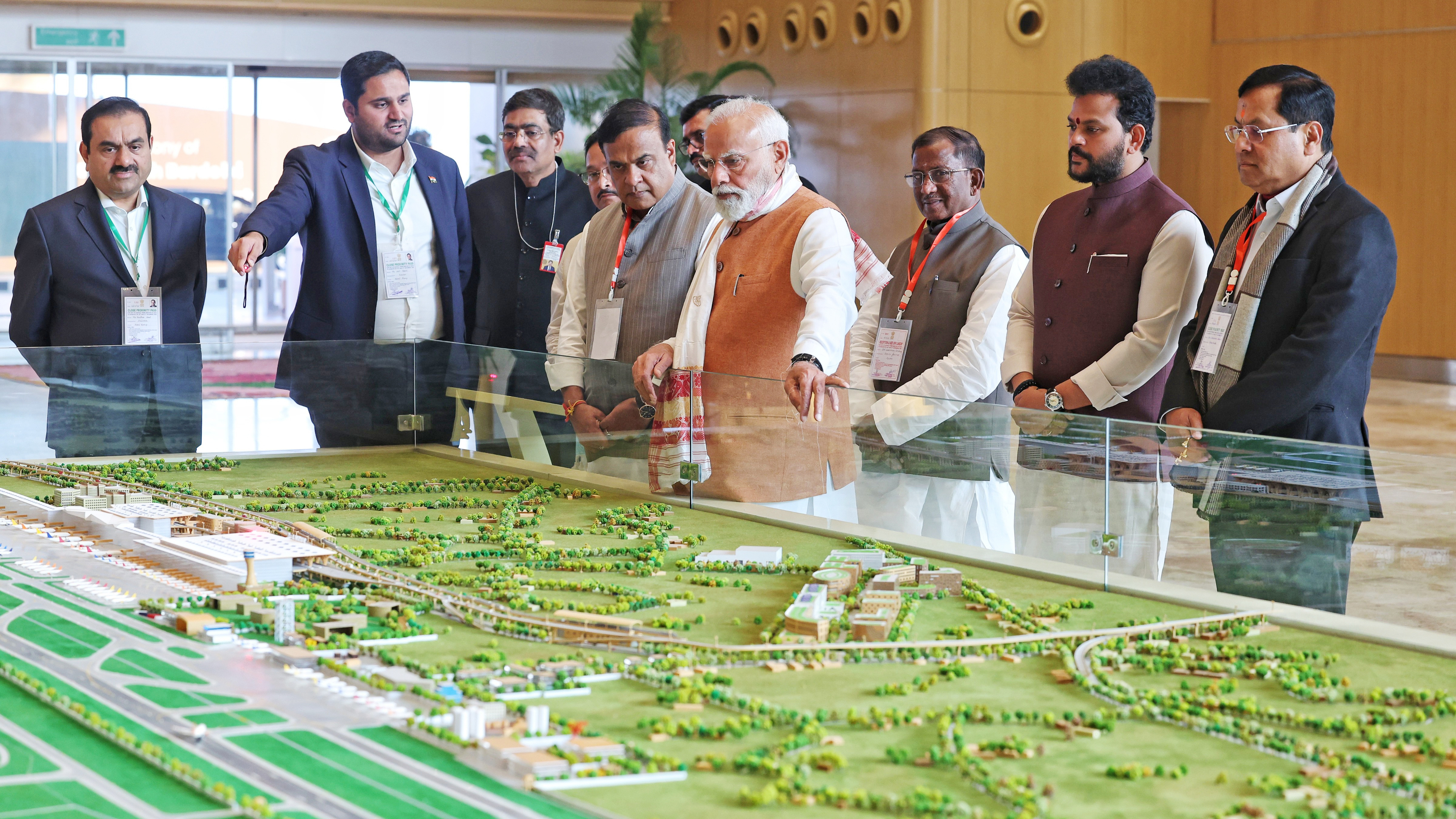 PM Modi, Gautam Adani, and officials inspecting a large airport model.